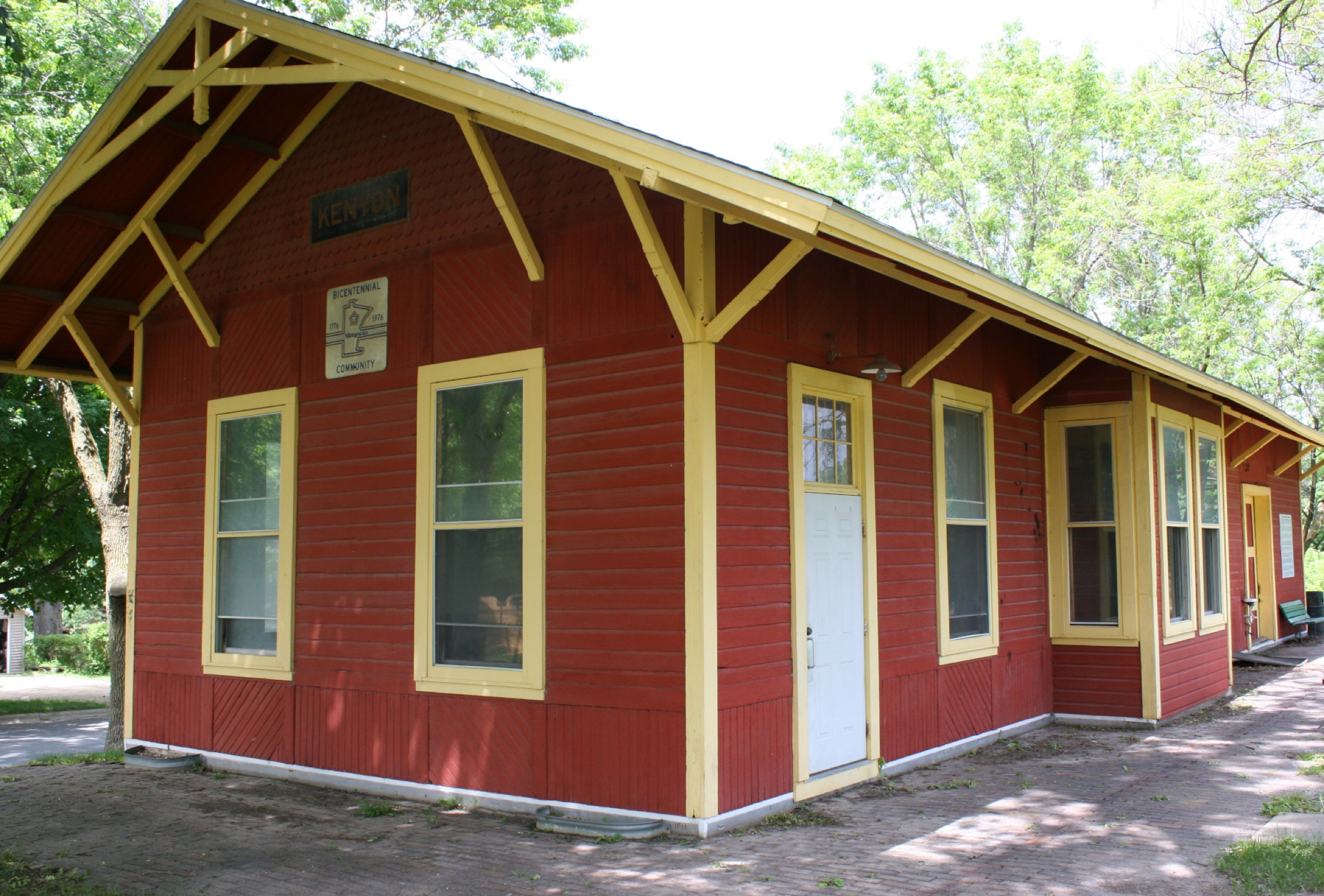 The red Chicago Great Western depot at Depot Park, Kenyon, with yellow trim and the KENYON station sign in the gable